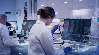 Scientist in a lab looking at a test tube in front of a computer screen